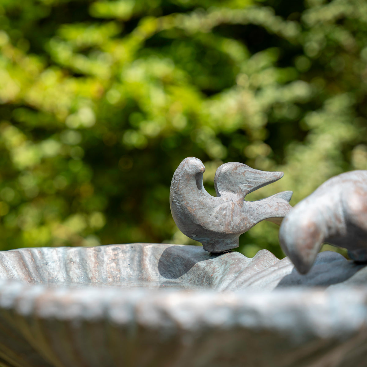 Decorative stone bird bath with two birds on top, set against a blurred green garden background.