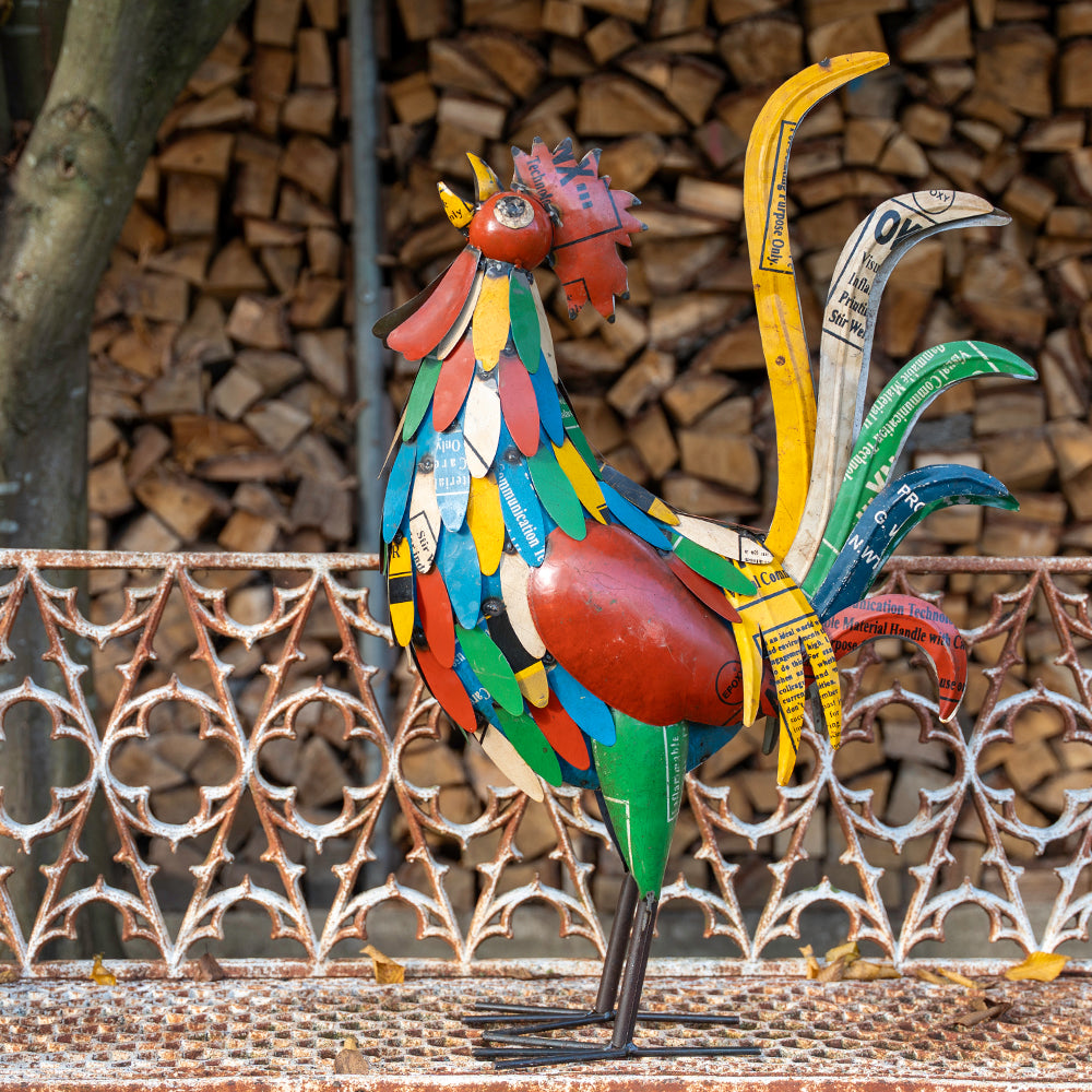 Colorful metal rooster sculpture in front of stacked firewood