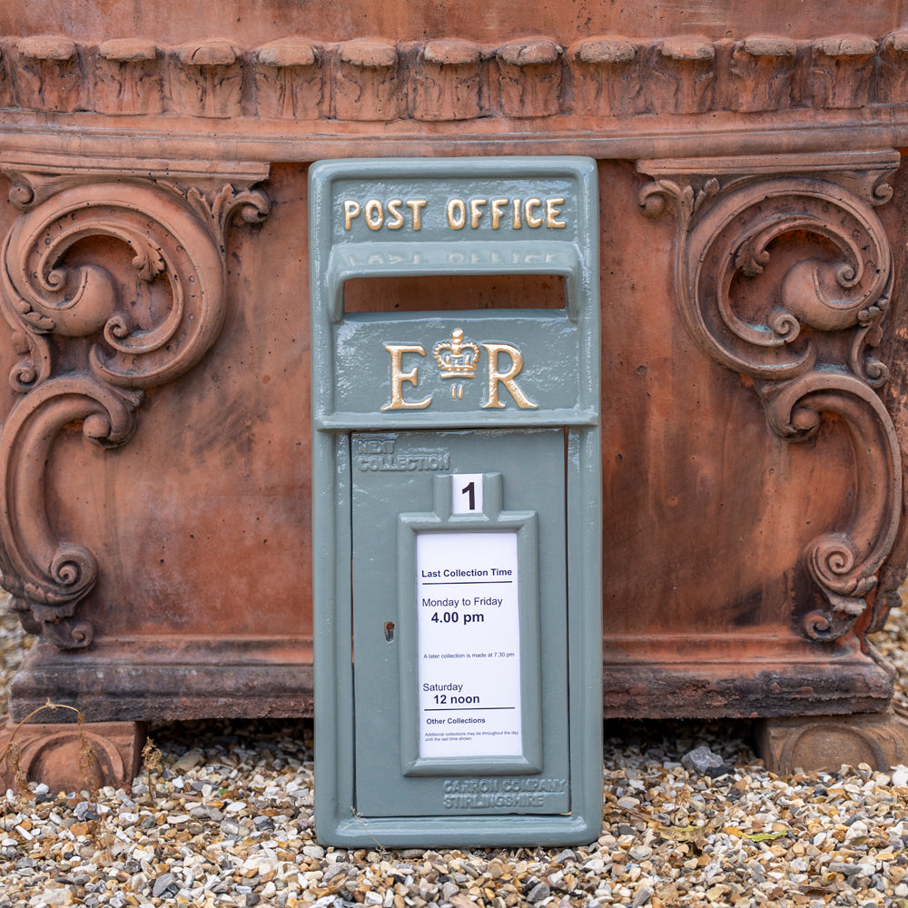 Vintage-style post box with 'POST OFFICE' and 'E R' branding against an ornate stone wall.