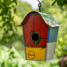 Red, blue, and yellow birdhouse with 'Epoxy' label hanging against a green leafy background