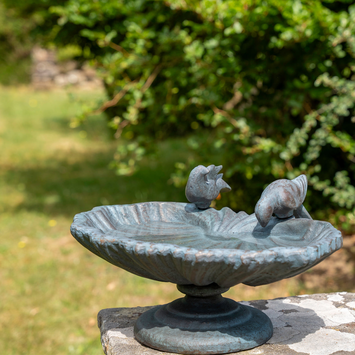Decorative garden birdbath with two bird statues on a stone ledge.