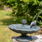 Decorative garden birdbath with two bird statues on a stone ledge.