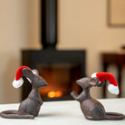 Two cast iron mouse figurines wearing Santa hats in front of a fireplace.