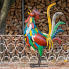 Colorful metal rooster sculpture in front of stacked firewood