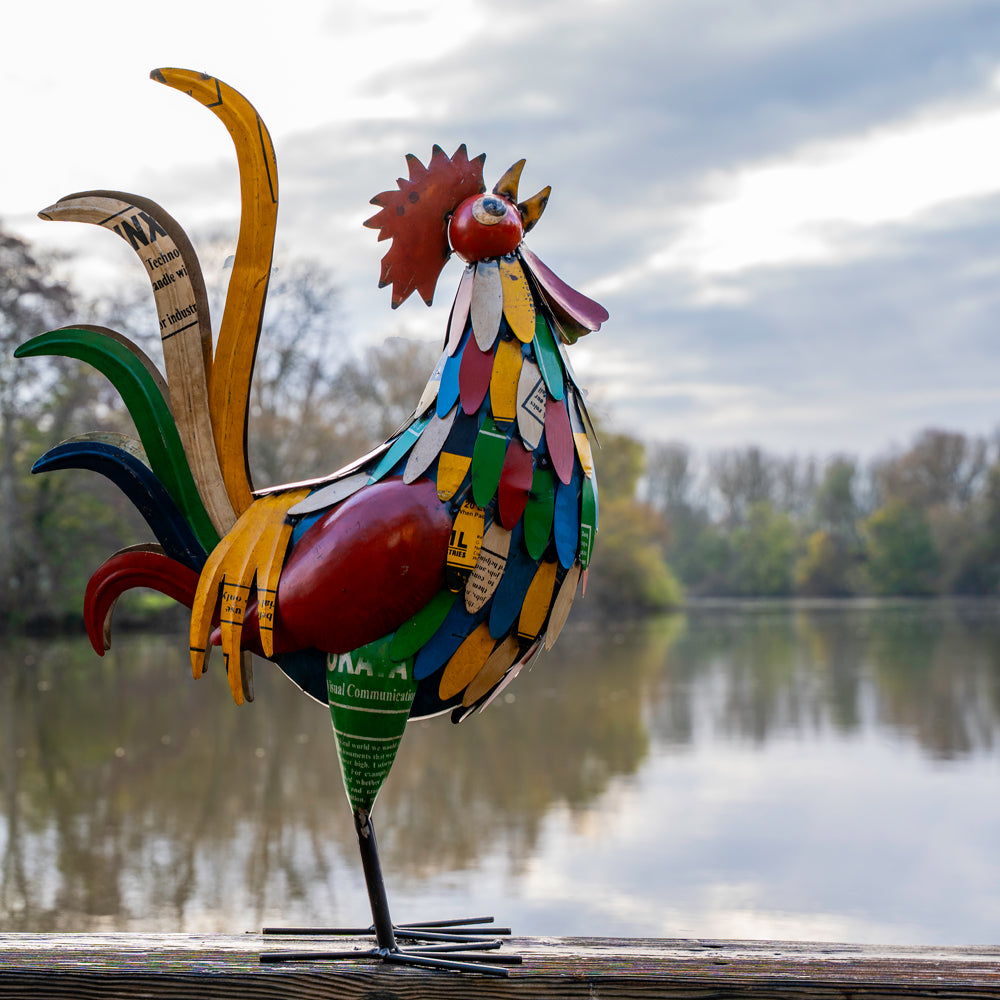 Colorful rooster sculpture on a wooden platform with a lake and trees in the background