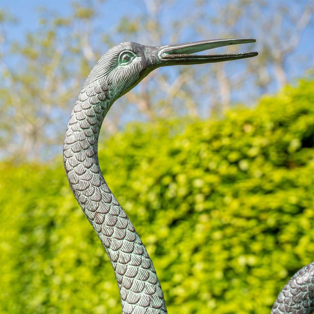Aluminium statue of a crane against a green hedge and blue sky background
