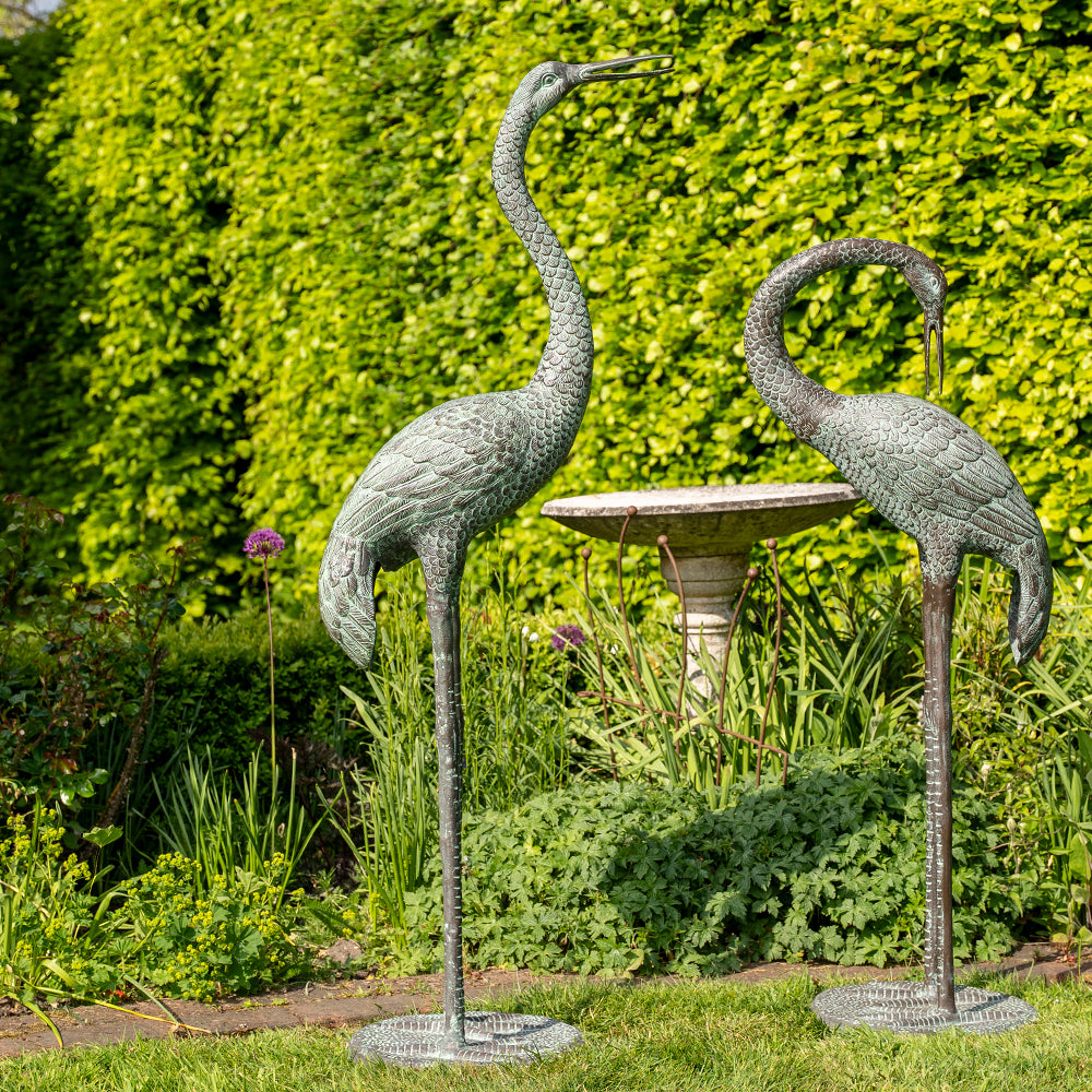 Two metal Crane sculptures in a garden setting with a bird bath.