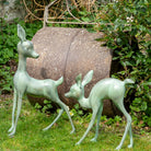 Two metallic deer sculptures in a garden setting with a stone barrel and greenery.