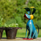 Colorful metal dog sculpture next to a potted plant outdoors
