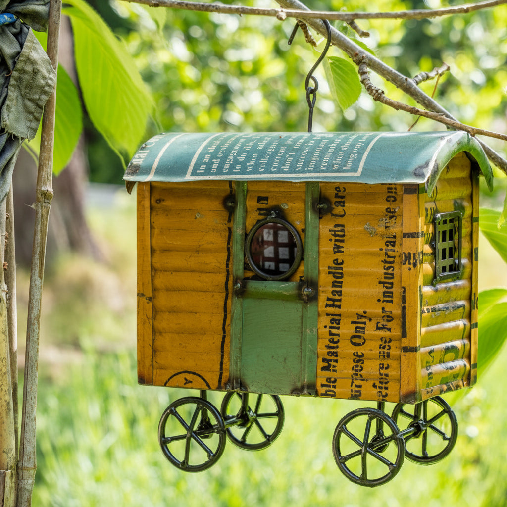 Decorative birdhouse resembling a shepherds hut hanging from a tree branch.