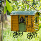 Decorative birdhouse resembling a shepherds hut hanging from a tree branch.