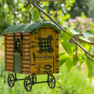 Decorative birdhouse resembling a small cabin with wheels, hanging from a tree branch.