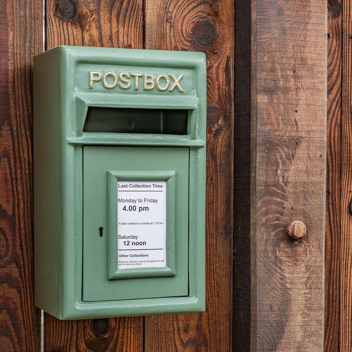 Green postbox with collection times displayed on a wooden wall