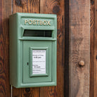 Green postbox with collection times displayed on a wooden wall