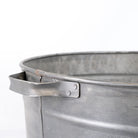Close-up of a galvanized metal bucket or tub with a flat metal handle attached near the rim, shown against a plain white background.