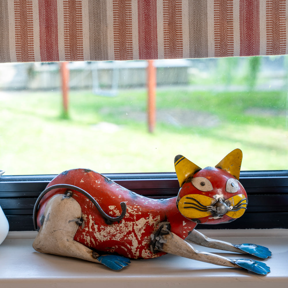 Red cat figurine with yellow ears on a windowsill with striped curtains