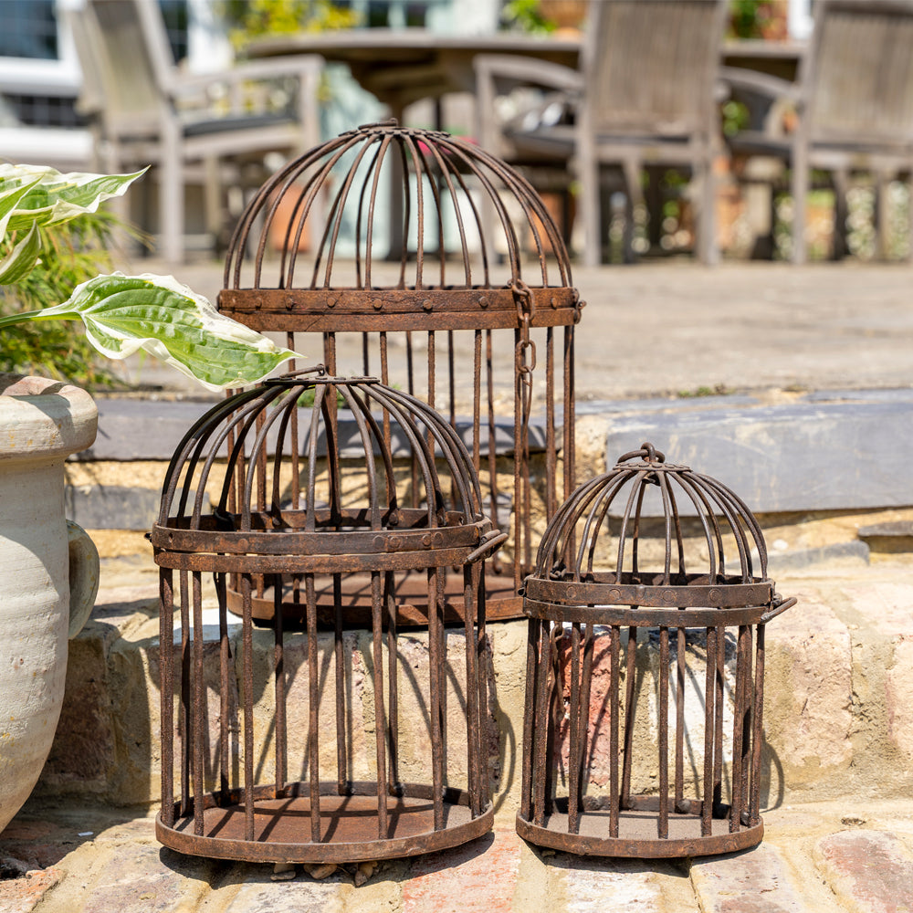 Three decorative metal birdcages on a stone surface with outdoor furniture in the background.