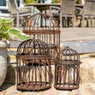 Three decorative metal birdcages on a stone surface with outdoor furniture in the background.