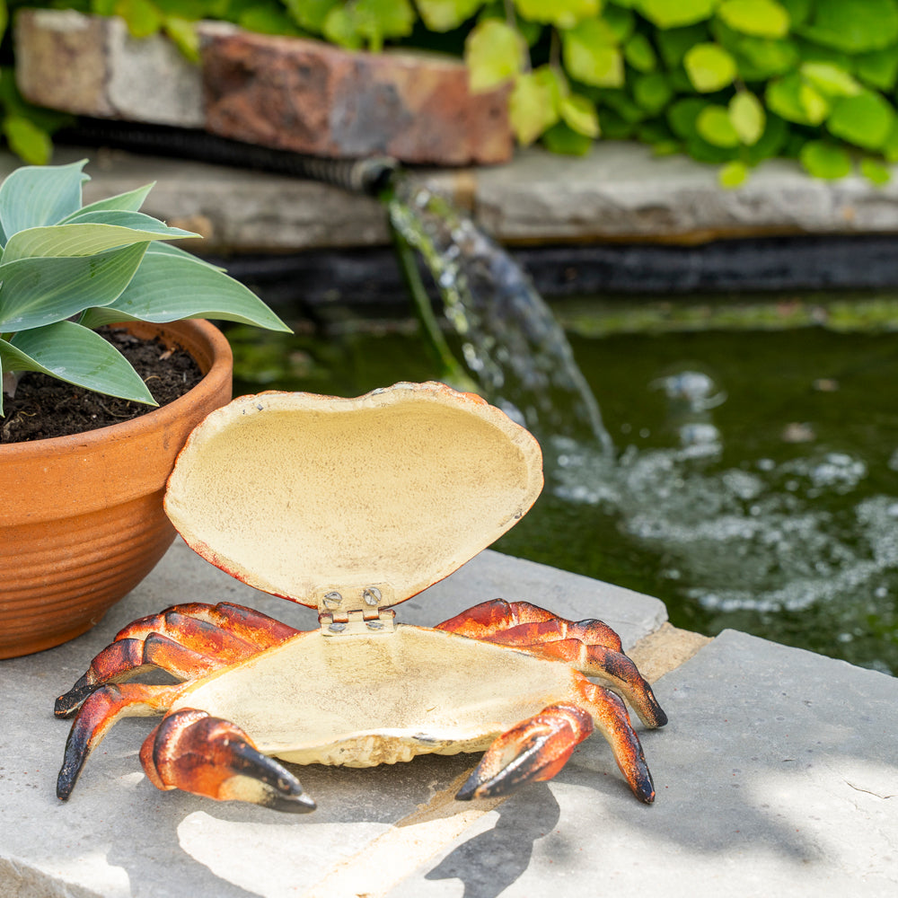 Decorative crab-shaped box on a stone surface with a garden background