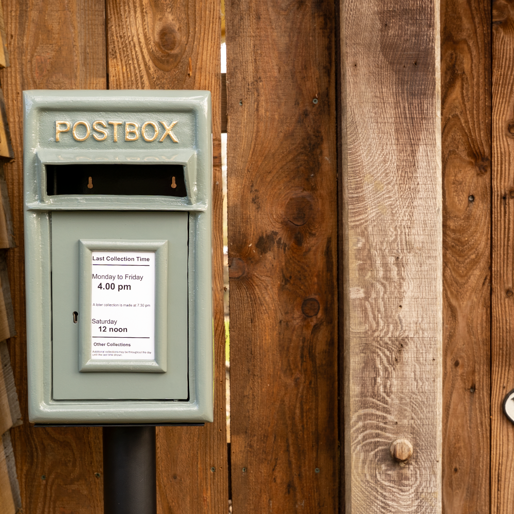 Traditional post box mounted on a stand with collection times displayed.