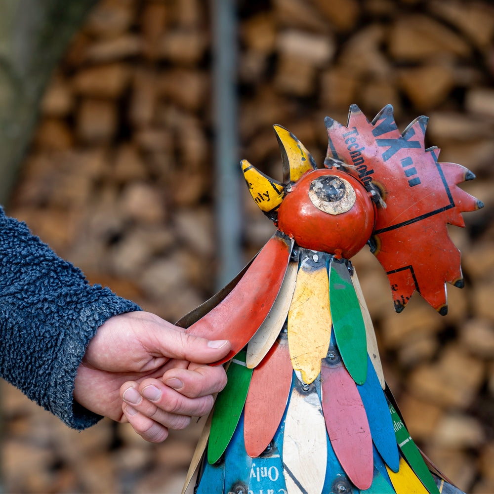 Colorful metal sculpture of a rooster held by a person against a blurred natural background