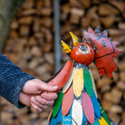 Colorful metal sculpture of a rooster held by a person against a blurred natural background